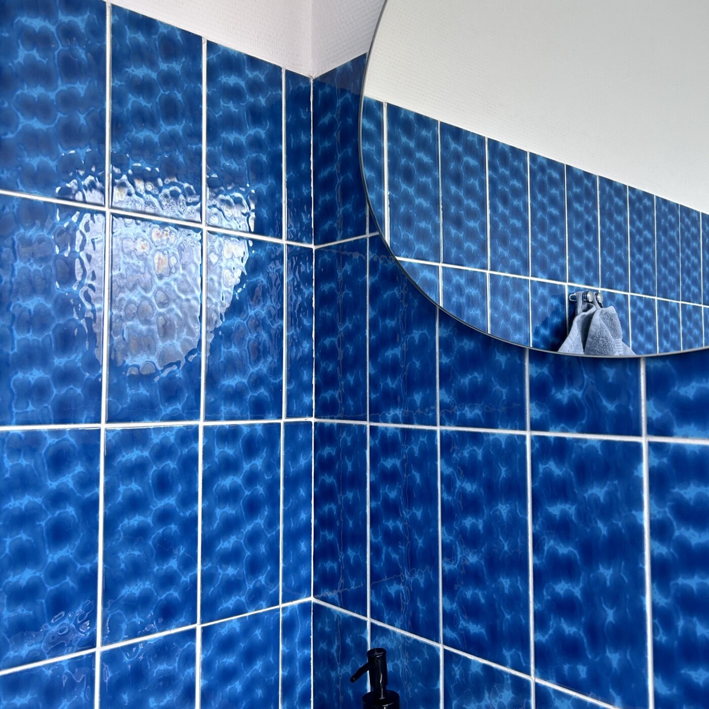 Udsnit af et badeværelse med himmelblå fliser og et rundt spejl.